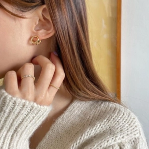 Close-up of gold interlocking hoop earrings and layered rings on model with knitwear