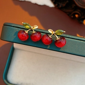 Macro shot of red cherry earrings with gold leaves and green stones on a jewelry box