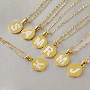 Macro shot of 18K gold plated circular initial pendants with white letter inlay details