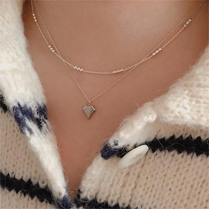 Double-layered gold necklace with round beads and geometric diamond pendant on a model