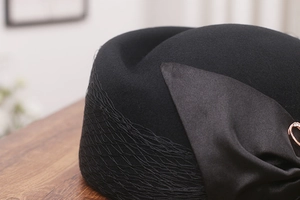 Close-up of black wool beret with mesh veil, satin bow, and gold heart brooch detail