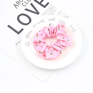 Close-up of pink Christmas hair scrunchie with red and green polka dots on white plate