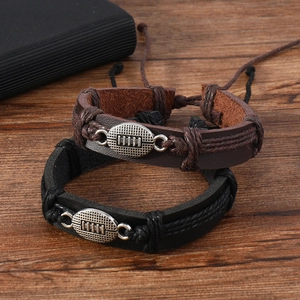 Set of brown and black braided leather bracelets with metal football charms on wood