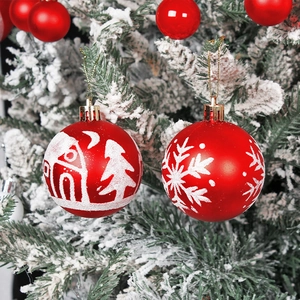 Red Christmas ball ornaments with white snowflake patterns hanging on a snowy Christmas tree