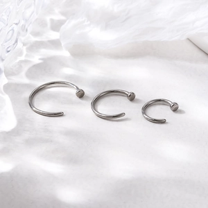 Three G23 titanium C-shaped nose rings in different sizes on an elegant white fabric