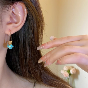 Detail view of gold hoop earring with light blue floral charm on a female model