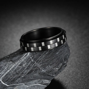 Detailed view of black titanium spinner ring with silver checkered pattern on dark rock
