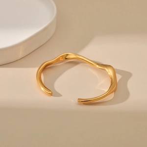 Vista detallada del brazalete dorado ondulado con un diseño minimalista y pulido