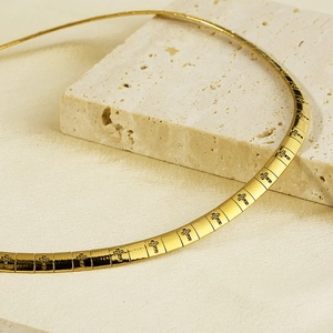 Golden 6mm flat chain necklace with black cross patterns displayed on travertine stone