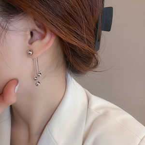 Close-up of a silver tassel earring with metallic beads worn by a model on a clean background