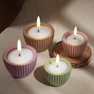Dettaglio di quattro candele profumate a righe colorate su una base di legno rustica