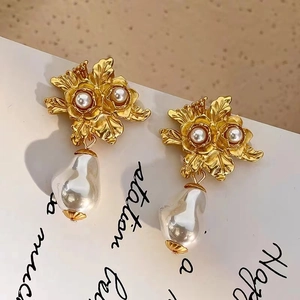 Gros plan de boucles d'oreilles fleur dorée avec perles baroques sur fond vintage