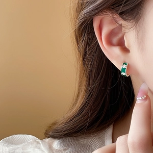 Detail of green enamel earring with white floral patterns on a female model