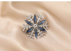 Macro shot of silver snowflake brooch with blue marquise crystals on champagne silk