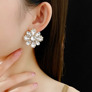 Detail of sparkling crystal flower earring set in gold metal worn by a female model
