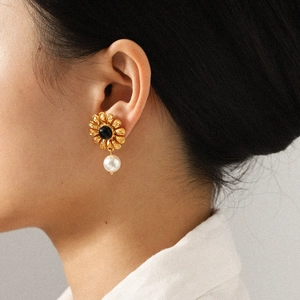 Golden flower earrings with black gemstone center and pearl drops on a model