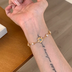 Detailed view of elegant gold daisy pearl bracelet featuring a blue zircon center on wrist.