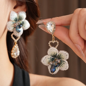 Détail de boucles d'oreilles vintage avec fleurs brodées blanches et perles bleues