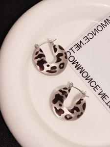 Detail view of C-shaped resin earrings with cow print pattern on white ceramic tray