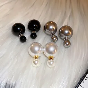 Three pairs of pearl stud earrings in white, grey, and black on soft plush fabric