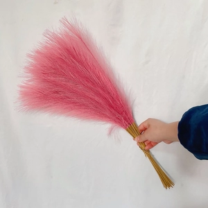 Close-up of fluffy pink faux pampas grass decor held against a clean white background