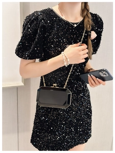 Detail of glossy black acrylic clutch with gold chain on sequined dress outfit