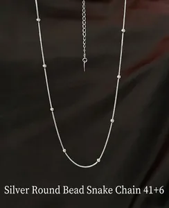 Detailed view of a silver snake chain necklace with beads on brown silk background