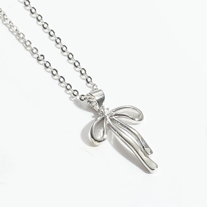 Close-up of silver bow pendant necklace with a sparkling central zircon on white background