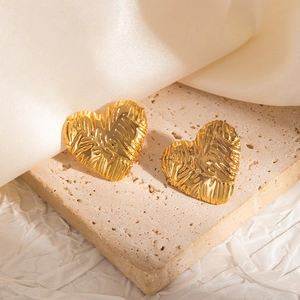 Detailed view of heart-shaped gold earrings with unique hammered texture on stone