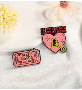 Detailed close-up of pink self-love enamel pins featuring a ticket and heart lock key