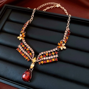 Detail of vintage gold necklace with red rhinestones and teardrop pendant on black tray
