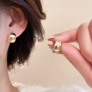 Close-up of elegant gold round stud earrings with a glossy mirror finish on the ear