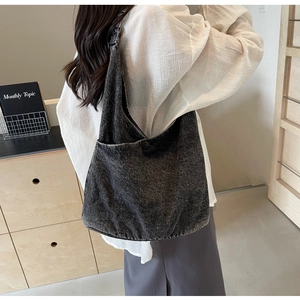Detail of a dark gray denim tote bag worn by a model, featuring a button closure