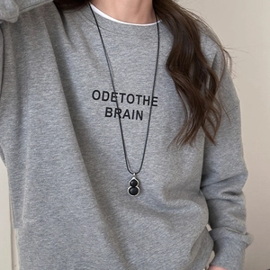 Detail of stone gourd pendant on long black cord necklace worn with grey hoodie