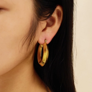 Close-up of model wearing thick twisted gold hoop earrings with irregular streamline design