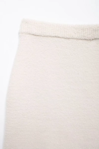 Detailed macro view of cream plush knit fabric texture and elastic ribbed waistband