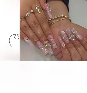Detail of pink press-on nails with 3D gold butterfly, white flowers, and glitter finish