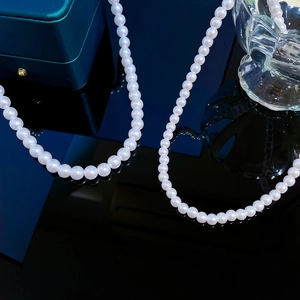 Lustrous white pearl necklace displayed on black reflective background with green gift box