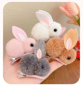 Gros plan de quatre barrettes lapin en peluche en blanc, rose, marron et gris sur bois