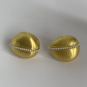 Dettaglio di orecchini a goccia in oro spazzolato con perle eleganti su sfondo bianco