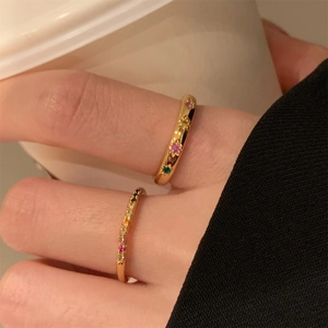 Dettaglio di anelli dorati con zirconi colorati indossati sulla mano su sfondo bianco