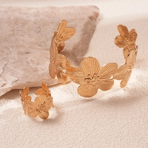 Macro detail of golden flower engraved bracelet and open ring set on natural stone background