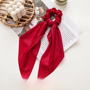 Close-up of a red pleated fabric Christmas hair scrunchie with long ribbon bow detail