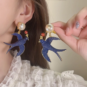Close-up of model wearing vintage blue swallow drop earrings with white pearl studs