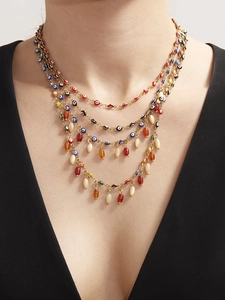 Detail van gelaagde gouden ketting met kleurrijke evil eye kralen en agaatdruppels op model