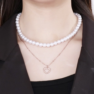 Detail of layered pearl necklace with rose gold chain and hollow heart pendant on neck