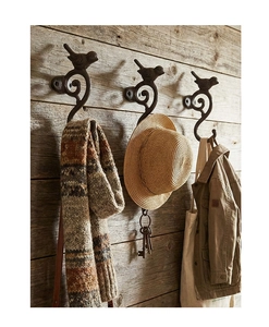 Detalle de tres ganchos de pared de pájaros en hierro fundido vintage sobre pared de madera