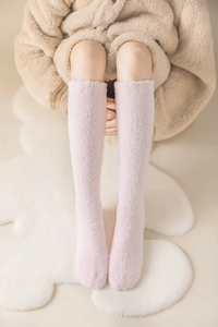 Detail view of pink knee-high coral fleece socks on soft carpet for winter warmth