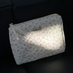 Detailed macro view of quilted cotton makeup bag with cherry print and brand tag