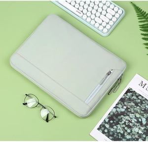 Light green laptop sleeve flat lay with zipper pocket, keyboard and office accessories